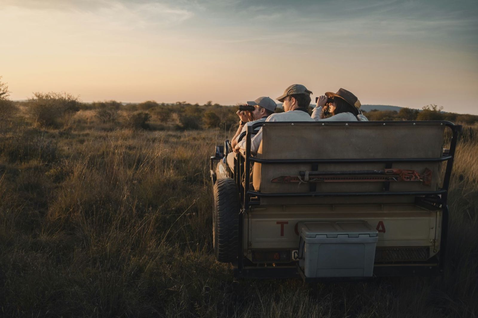 Travellers on a game drive in an open safari vehicle at dusk