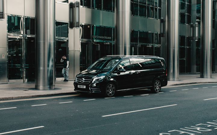 Black executive van parked outside a glass office building